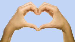 A pair of hands in a heart shape against the blue sky